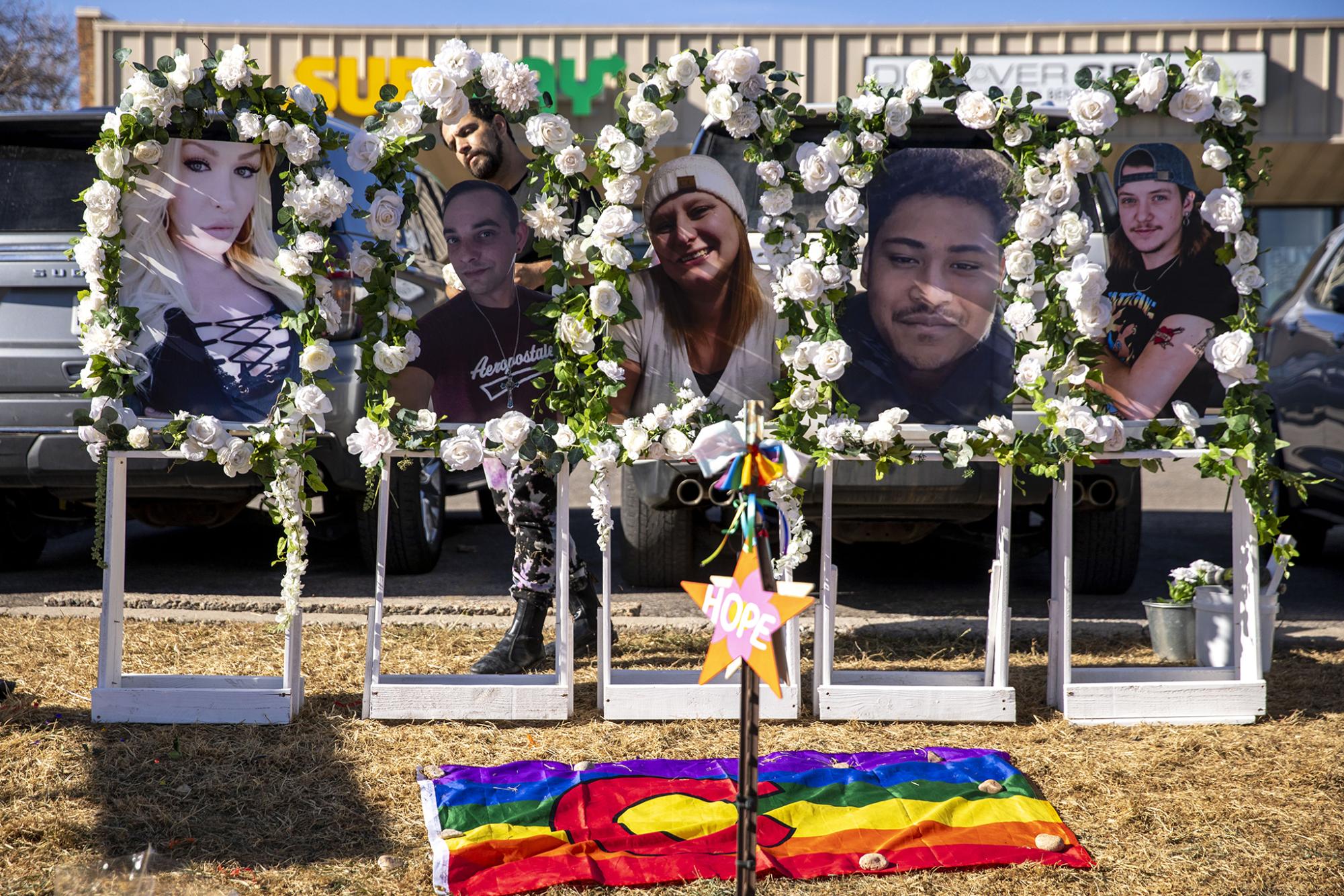 Photos of Kelly Loving (left to right), Derrick Rump, Ashley Paugh, Raymond Green Vance and Daniel Aston stand above a memorial outside of Colorado Springs Club Q. Nov. 22, 2022.